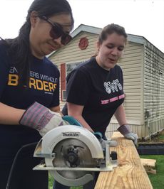 Elizabeth Dang and Kristy Rumball work together to cut a board for a wheelchair ramp.