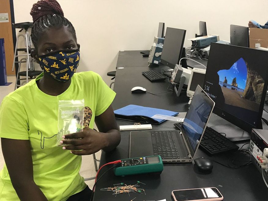 Black female student wearing a mask, works remotely from a computer lab