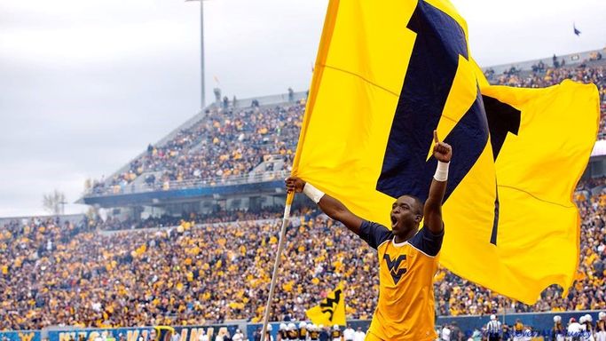 Lionell Marshall carrying the "W" flag on the field at Mylan Puskar Stadium in Morgantown.