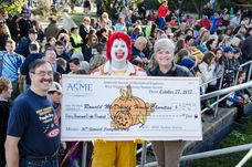 Ronald McDonald holding a large pumpkin check showing the donation being made to Ronald McDonald House.