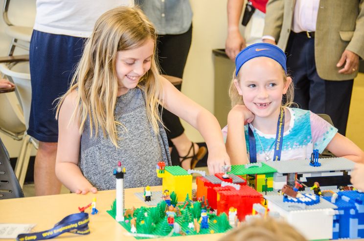 A photo of two girls building a city out of Legos.