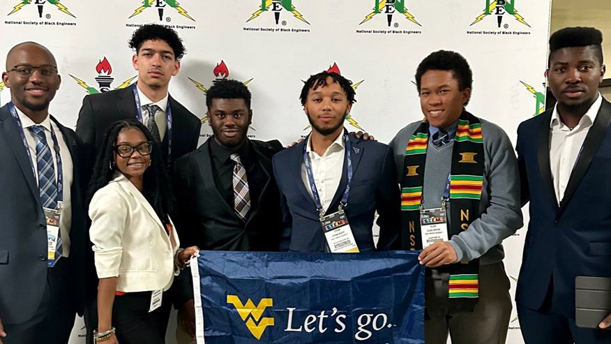 WVU NSBE students standing in front of a backdrop holding a West Virginia University banner that says Let's Go