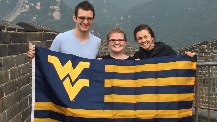 Andy Maloney, Emily Phipps and Katie O'Connell pose together holding the West Virginia University flag on top of the Great Wall of China