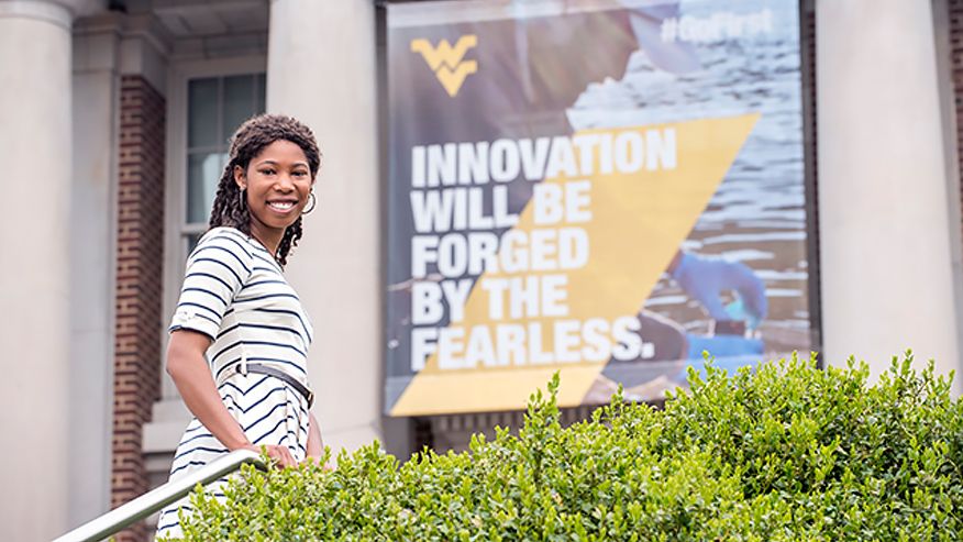 Noelle Honey cut standing in front of a WVU sign "Innovation will be forged by the fearless."