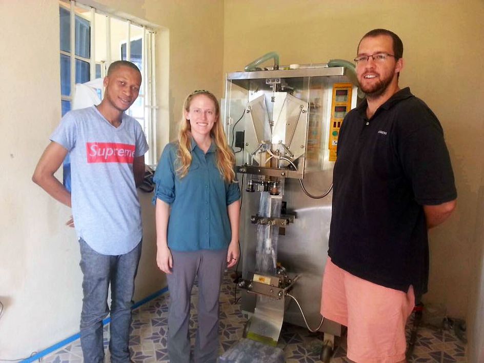 Kolar and Asher are seen with the water packing device used at the Sola Wata Water Packaging Center in Sierra Leone.