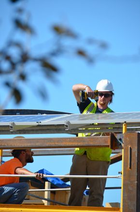 An image of one of the Solar Team members using a power drill on the roof of the Solar House to fixate two adjoining sections.