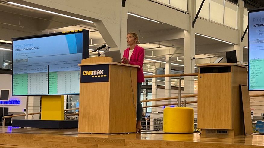 Kimberly Morris on stage at CarMax headquarters delivering a presentation on two projector screens. 