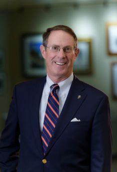Portrait photo of person in blue suit with striped tie and glasses