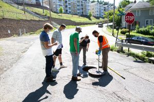 Members of the WVU COVID-19 wastewater testing team prop open a manhole cover near student housing to collect a wastewater sample. Pictured (left to right) are Eric Lindstrom, an epidemiology doctoral student; Zheng Dai, an epidemiology postdoctoral resea
