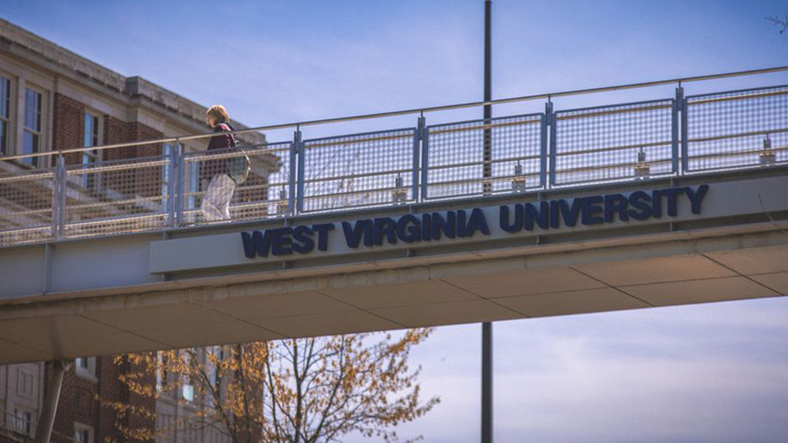 Student on walkway bridge labeled 'West Virginia University'