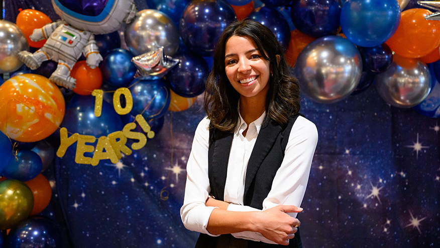 Emily Certain in front of a starry party background with planet and astronaut balloons celebrating 10 years