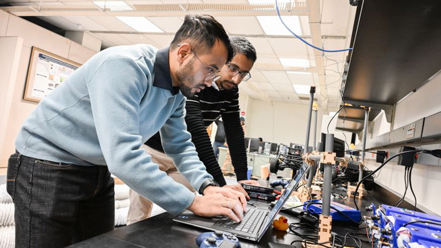 Students working in lab stand over computer screen with wires and controllers on table around them