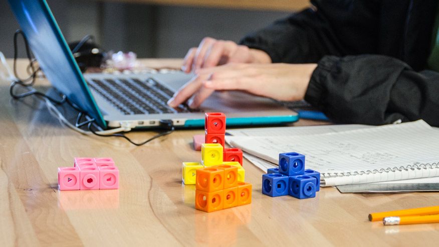 Person working on a computer with building blocks next to them.