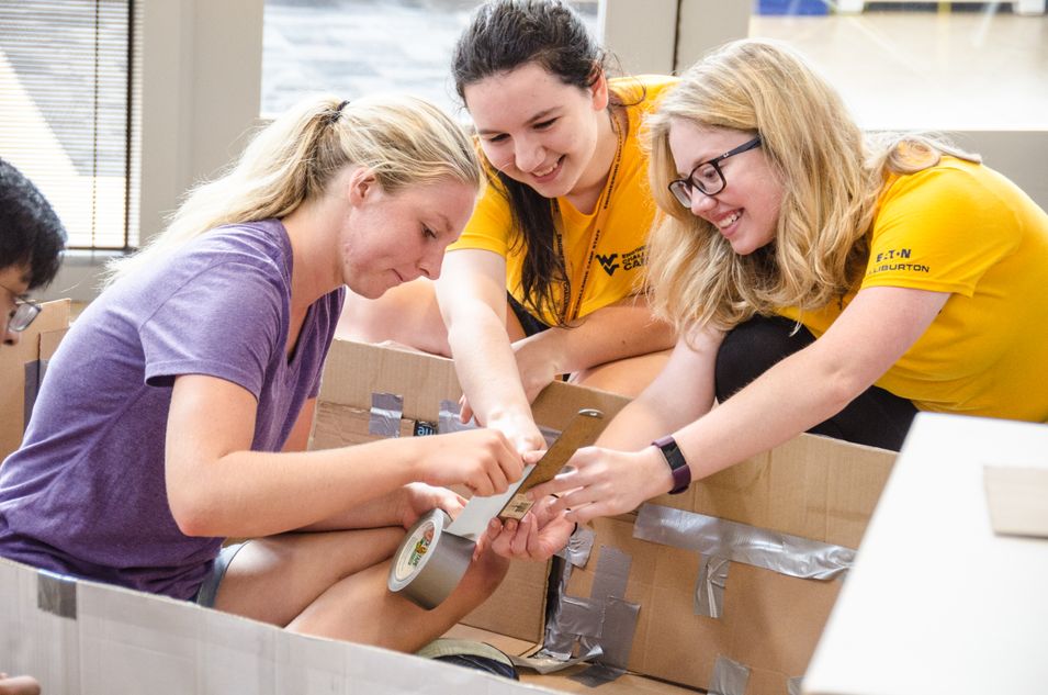 Two counselors help high school students build cardboard canoes. 
