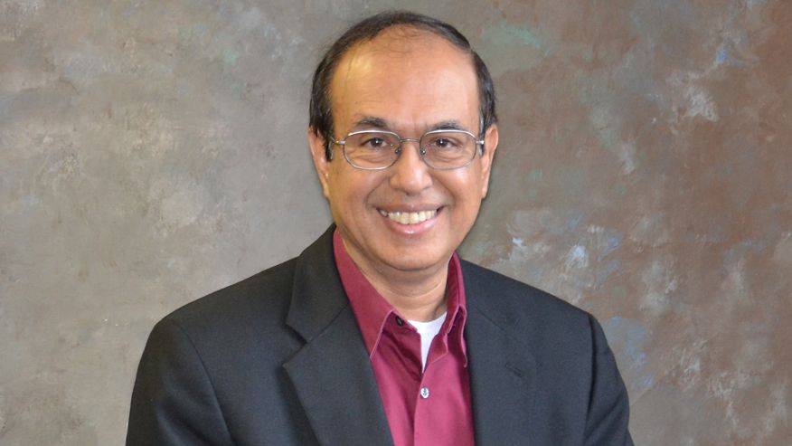 A portrait of Rakesh Gupta in a charcoal colored suit and a burgundy dress shirt.